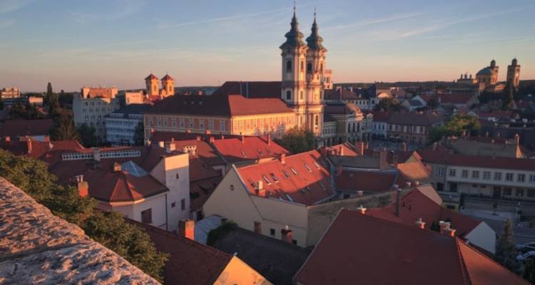 Scenic view of Eger's rooftops with churches and a sunset sky.