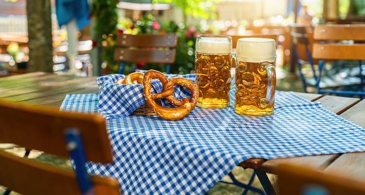 Tisch mit Brezeln und Bierkrügen in einer Außenumgebung.