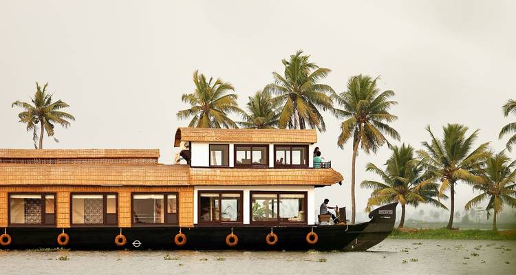 Croisière traditionnelle en bateau-maison du Kerala passant devant des cocotiers sur les eaux calmes des backwaters.