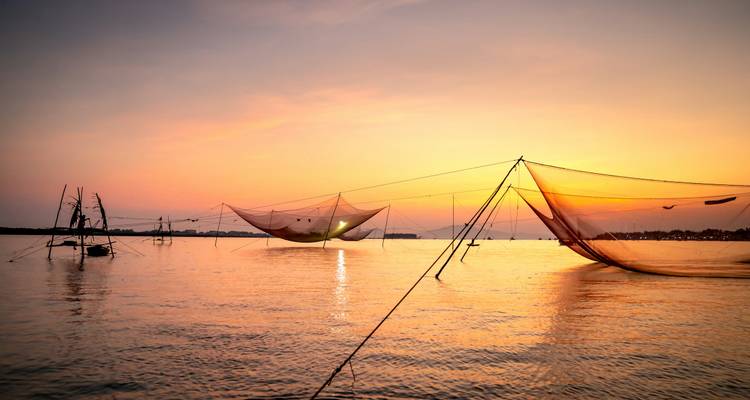 Les filets de pêche chinois se découpent en silhouette au-dessus de l'eau scintillante lors d'un coucher de soleil d'un orange vibrant.