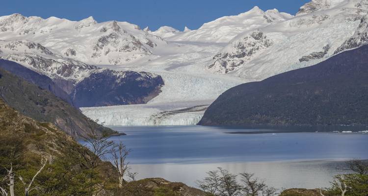 Un vaste glacier descendant dans un lac bleu avec des montagnes enneigées environnantes.