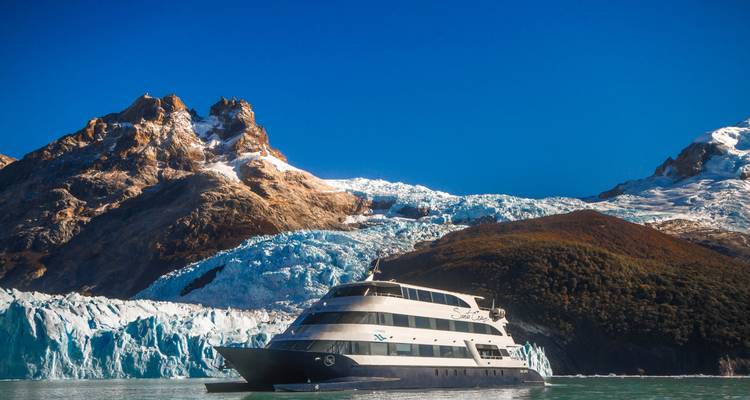 Bateau naviguant près d'un glacier avec des sommets enneigés.