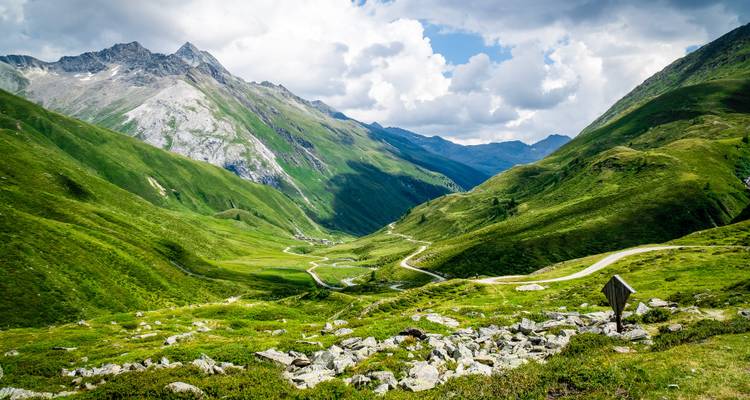 Üppiges grünes Tal mit gewundener Straße und hohen Bergen.