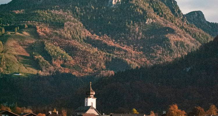 Kerktoren met beboste bergen op de achtergrond.