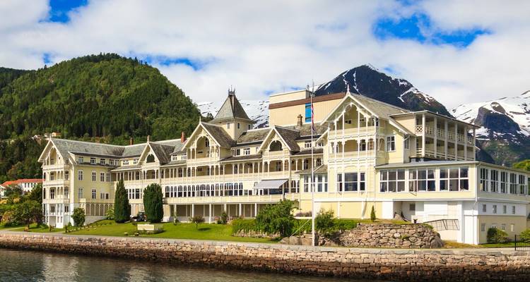 Grand hôtel historique en bois avec une toile de fond alpine aux abords d'un fjord tranquille