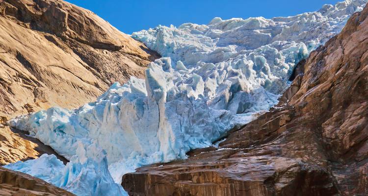 Blue-tinted glacier with rugged rock formations under clear sky.