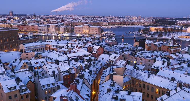 Paysage urbain hivernal avec des toits enneigés et une rivière.