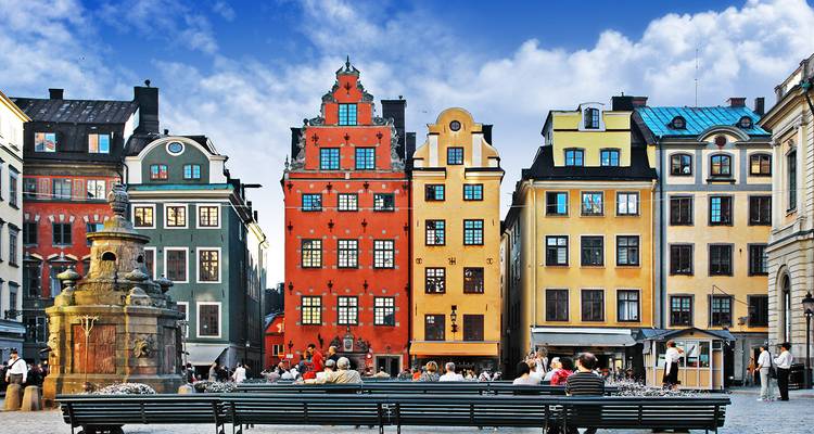 Place de ville animée avec des bâtiments colorés et des gens assis.
