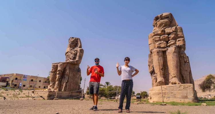 Les voyageurs saluent à côté des colosses colossaux de Memnon sous un ciel désertique dégagé.
