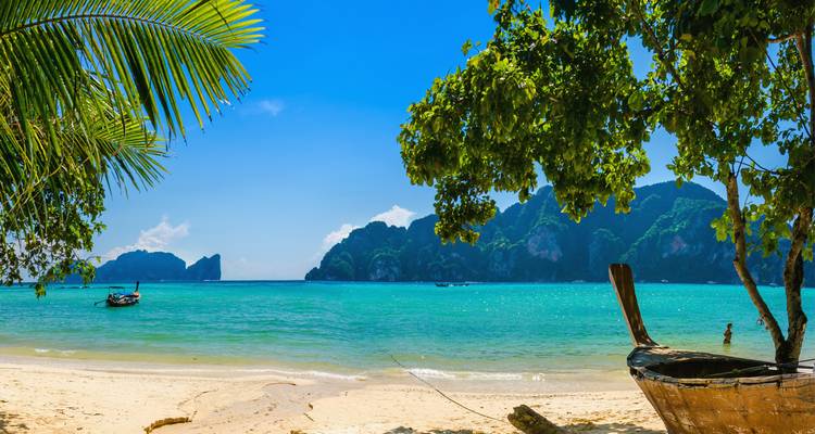 Tropical beach with boats, turquoise water, and limestone cliffs.