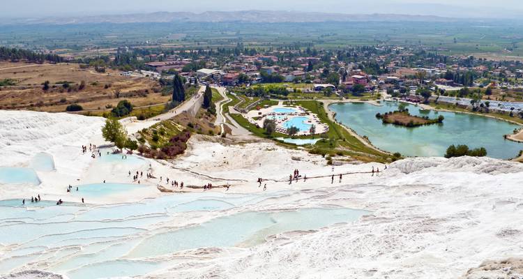 Weiße Terrassen von Pamukkale mit Becken und Ruinen im Hintergrund.