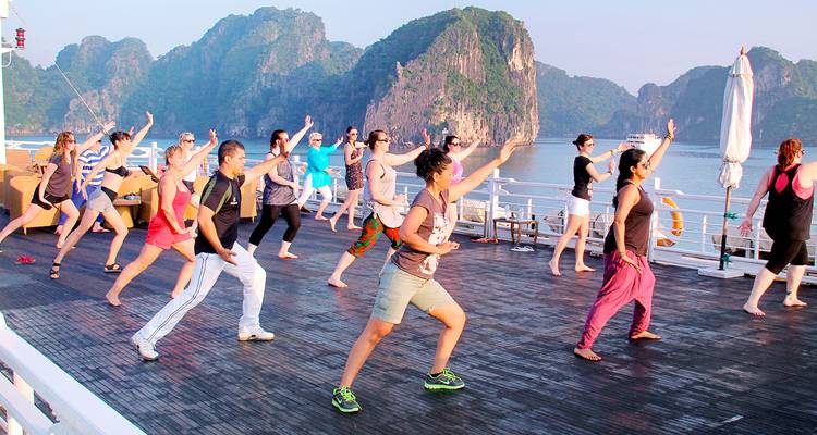 Menschen, die Tai Chi auf einem Boot praktizieren, mit Karstbergen im Hintergrund.