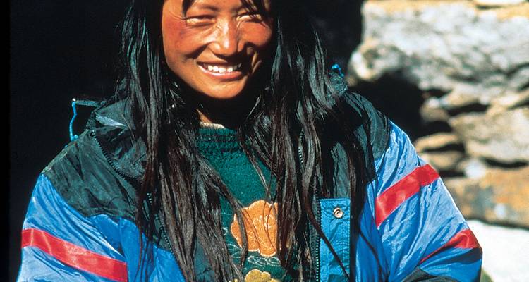 Femme bhoutanaise souriante portant une veste, éclairée par la lumière du soleil.