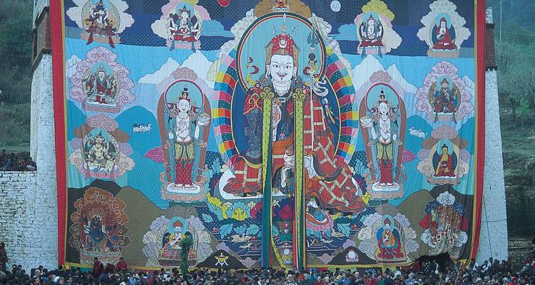 Énorme thangka de Guru Rinpoché déployé sur un mur de monastère avec des foules rassemblées en contrebas.