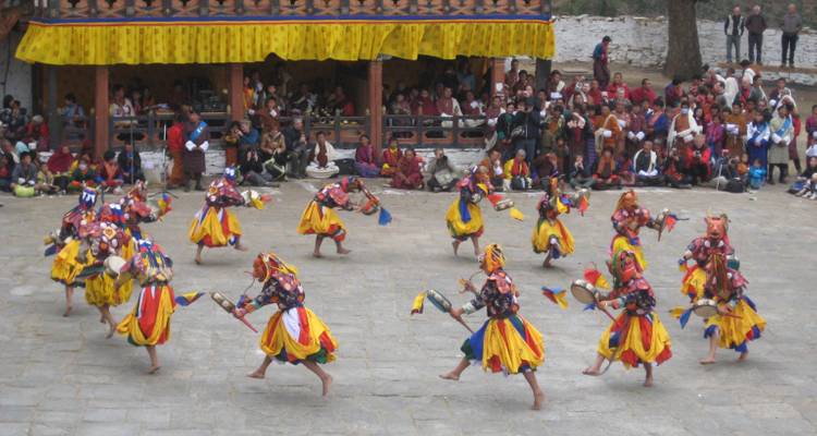 Des danseurs masqués bhoutanais se produisent en costumes colorés lors d'un festival dans une cour d'honneur devant un large public.