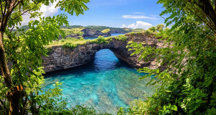 Un arco natural sobre un mar turquesa, rodeado de vegetación exuberante.