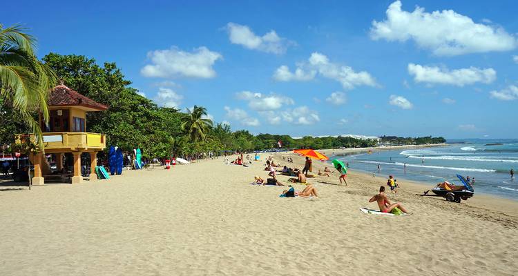 A busy sandy beach with people sunbathing and colorful umbrellas.