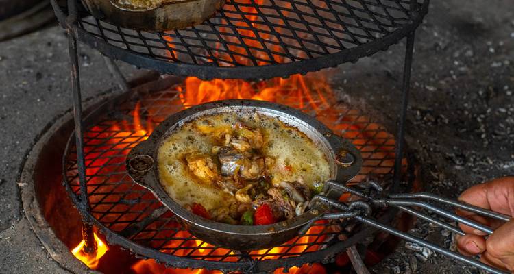 Food cooking on an open flame with visible hands holding a pan.