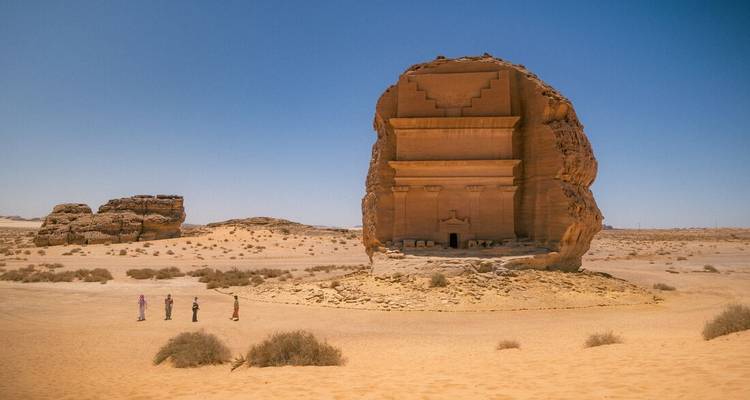 Ancient rock structure in a desert landscape with people in the distance.