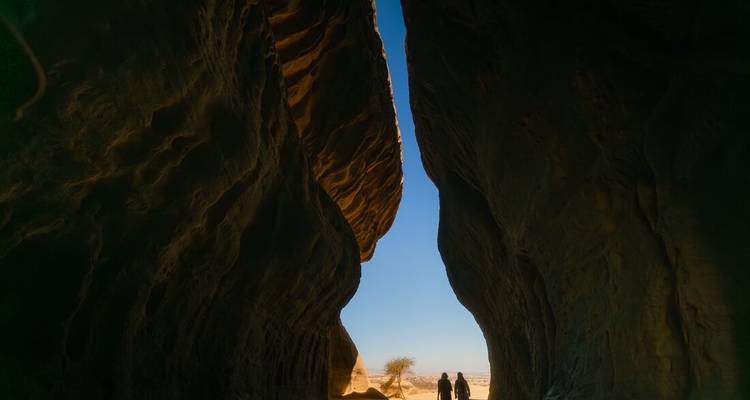 Silhouette of two people in a cave with a view of the landscape outside.