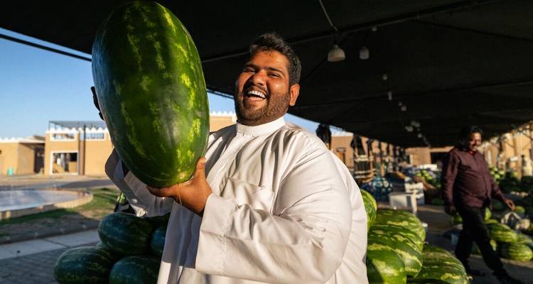 Man holding a large watermelon, smiling at a market.