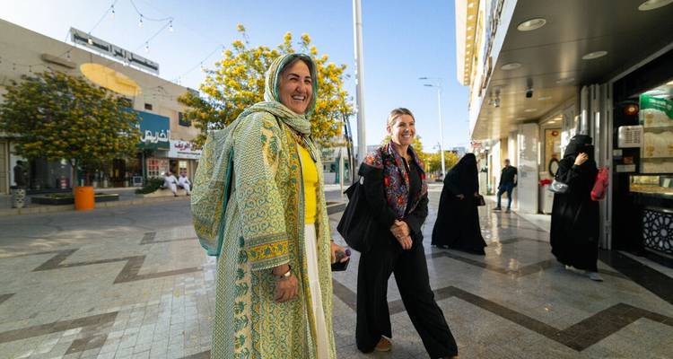 Femmes marchant dans une rue de marché avec des étals locaux.