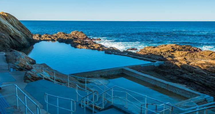 Piscine naturelle rocheuse avec accès par escalier et la mer en arrière-plan.
