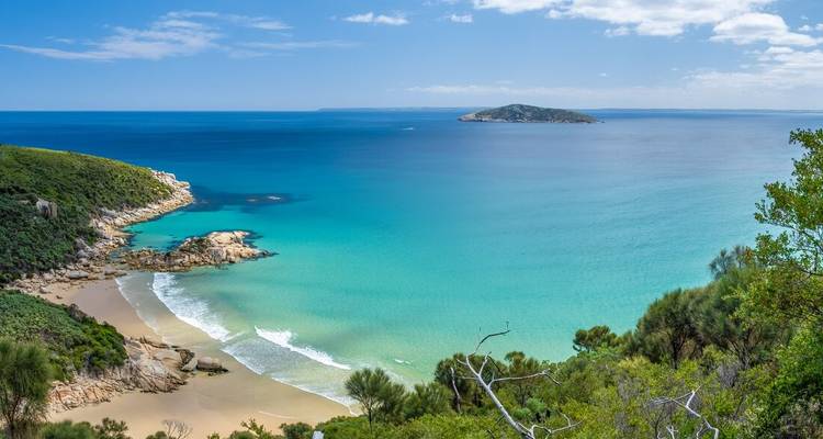 Baie turquoise avec plage de sable et promontoire verdoyant.