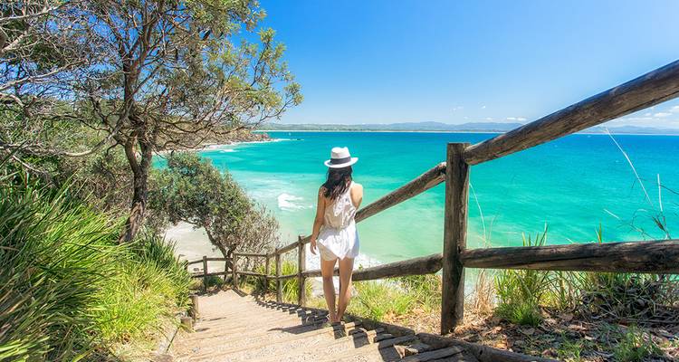 Femme descendant des marches vers un océan turquoise.