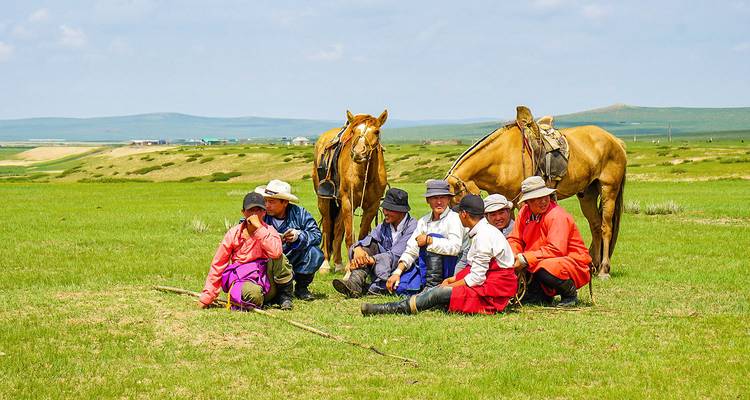 Groupe de personnes en tenue traditionnelle assises dans un champ avec des chevaux.