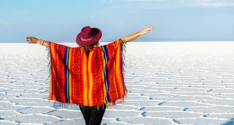 Person with outstretched arms in colorful garment on salt flats.