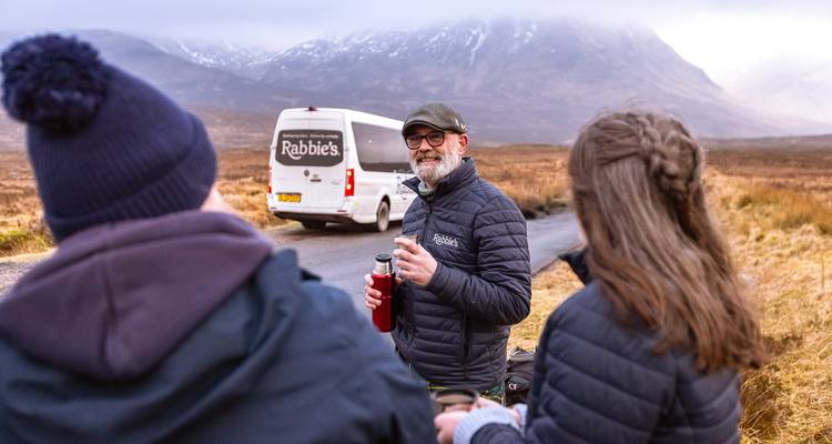 Group of people standing near a tour van with misty mountains in the background.