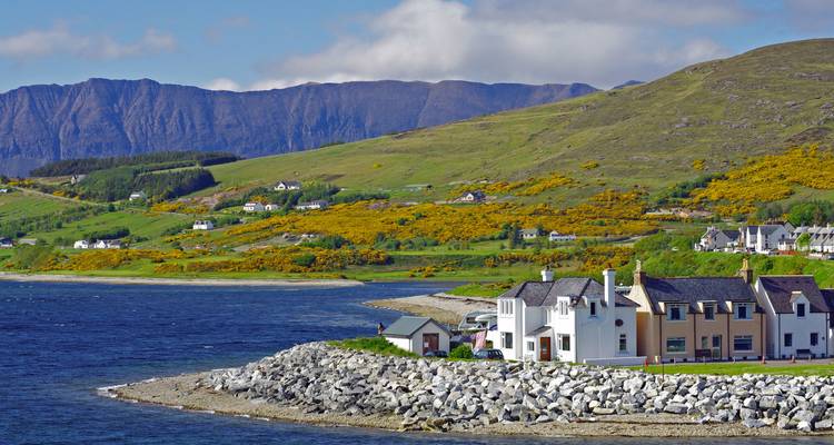 Coastal village with rocky shoreline and mountains in the background.
