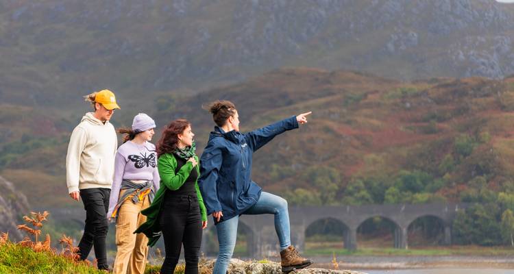 Group of people exploring a Scottish landscape near a viaduct.