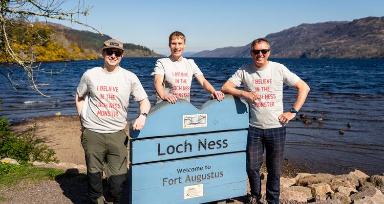 Group of people wearing 'I believe in the Loch Ness Monster' t-shirts at Loch Ness.