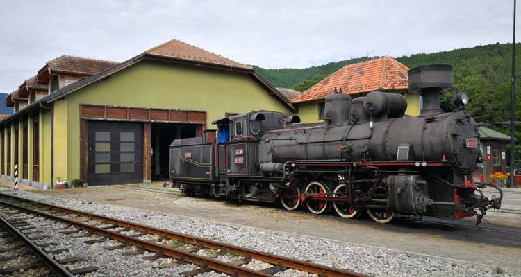 Locomotive à vapeur historique devant un dépôt ferroviaire.