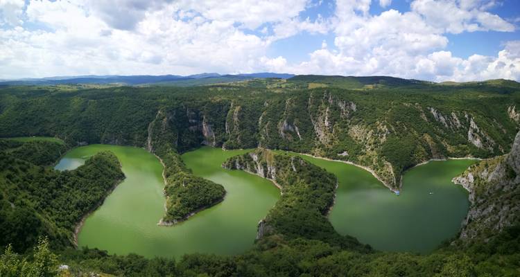 Une rivière sinueuse entourée d'une forêt verdoyante sous un ciel partiellement nuageux.