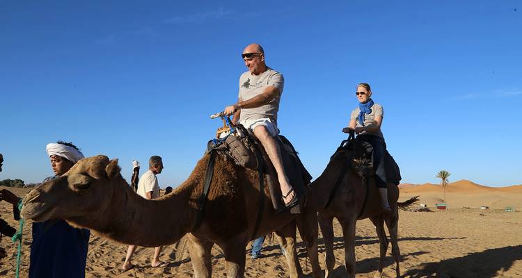 Des gens montant des chameaux dans un désert sous un ciel bleu clair.