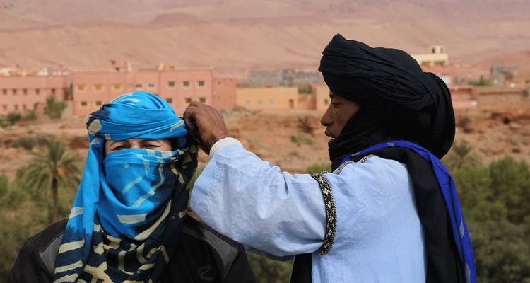 Un homme en tenue traditionnelle ajustant un foulard pour une autre personne.