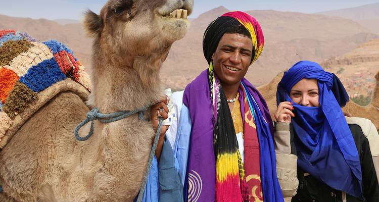 Deux personnes posant avec un chameau en tenue colorée.
