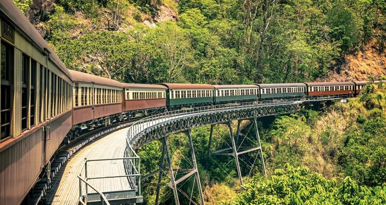 Oldtimer-Zug auf einer Brücke in üppig grüner Berglandschaft.