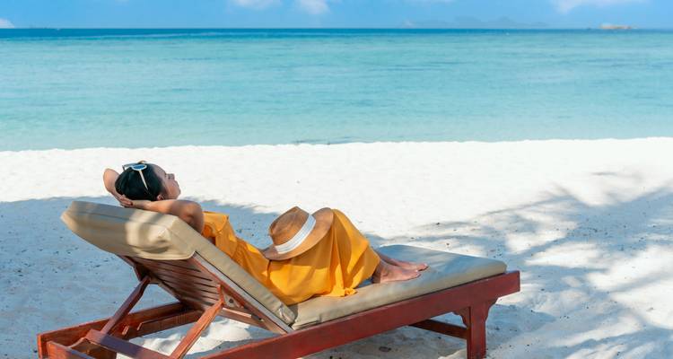 Personne se relaxant sur une chaise de plage face à la mer sereine.
