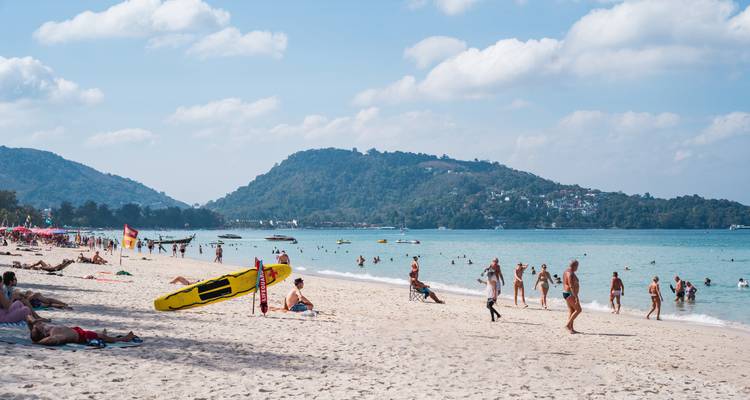 Plage bondée avec des gens pratiquant diverses activités aquatiques.
