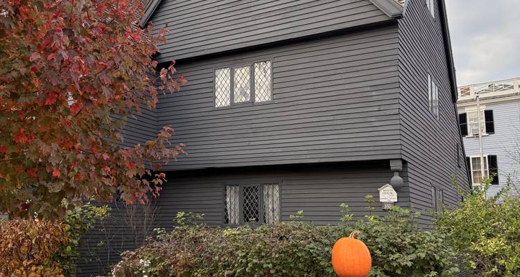 Une maison en bois sombre avec des feuilles d'automne et une citrouille à l'extérieur.
