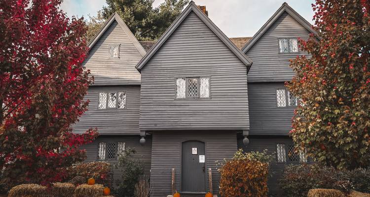 Une maison historique en bois avec des feuilles d'automne et des citrouilles à l'extérieur.