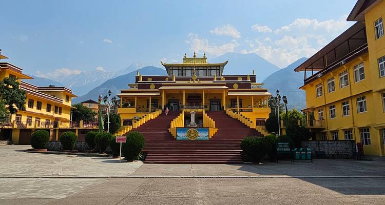 Monasterio budista pintado de amarillo con picos de montaña elevándose detrás bajo cielos despejados