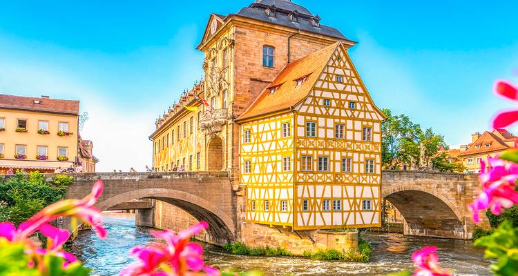 Picturesque view of a traditional building over a river with flowers in the foreground.