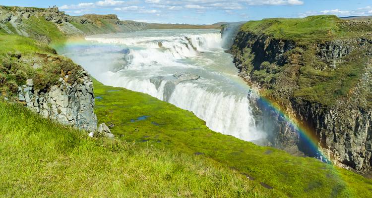 Wasserfall mit einem Regenbogen über üppigen grünen Klippen.
