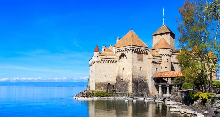 Le château de Chillon au bord d'un lac pristine sous un ciel bleu clair.