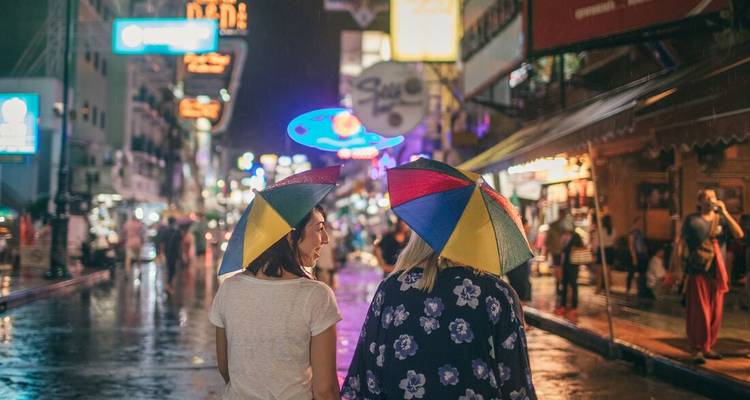 Deux personnes portant des parapluies colorés dans une rue animée la nuit.